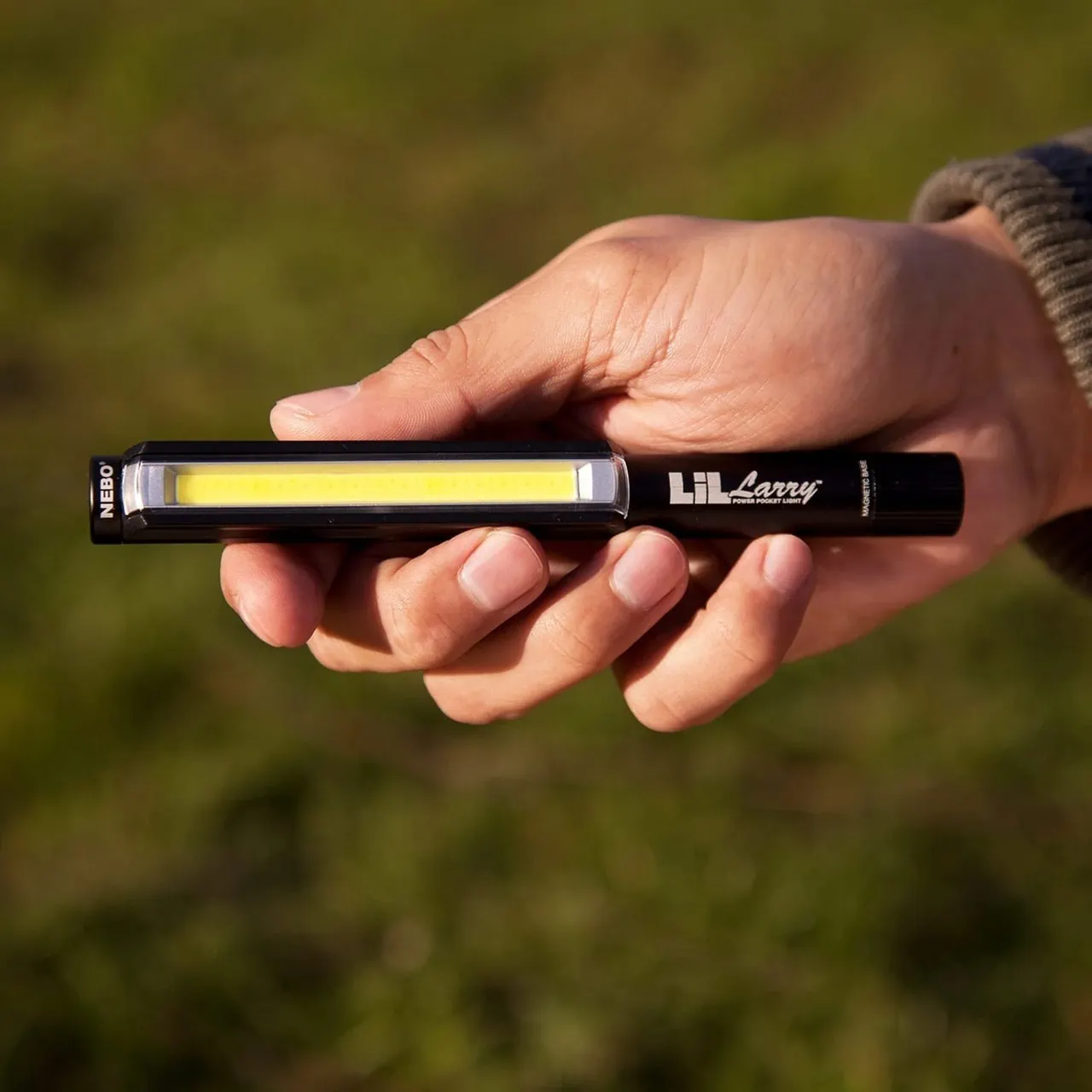 Nebo Lil Larry pocket light held in a person's hand against a blurred green background