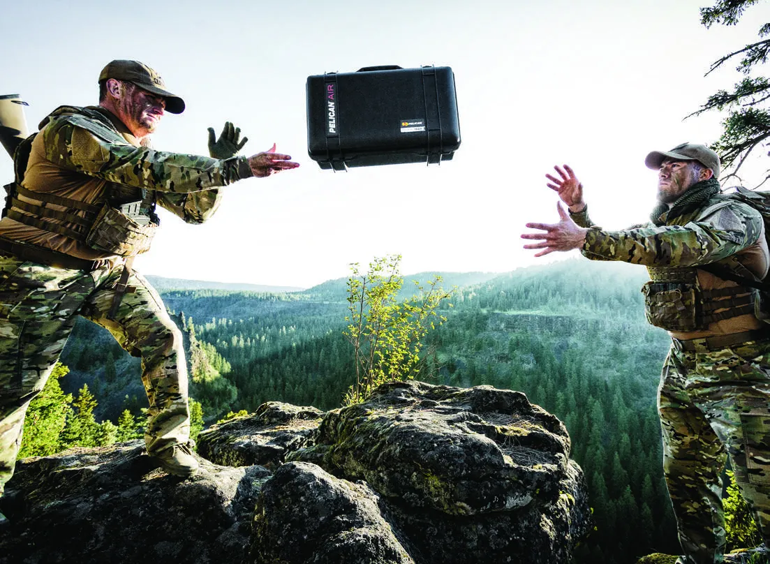 Pelican Air case thrown between two people on a mountain ridge